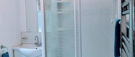 Ein modernes Badezimmer mit einer Duschkabine aus Glas, einem weißen Waschbecken und einem Spiegel.