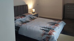 A bedroom with a bed, a nightstand, a dresser, and a door. - Knotty Ash - 3 Beds - Sleeps 6 - On-Site Parking (Liverpool)