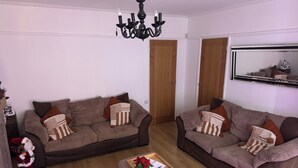 A living room with two brown sofas, a wooden coffee table, a chandelier, and a mirror on the wall. - Knotty Ash - 3 Beds - Sleeps 6 - On-Site Parking (Liverpool)