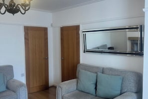 Ein Zimmer mit einem grauen Sofa, Holztüren und einem großen Spiegel an der Wand.