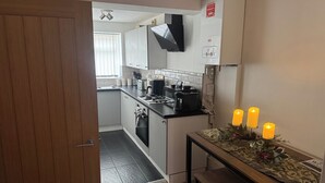 A compact kitchen with a stove, microwave, and a coffee maker. There is a table with candles and a decorative table runner. - Knotty Ash - 3 Beds - Sleeps 6 - On-Site Parking (Liverpool)