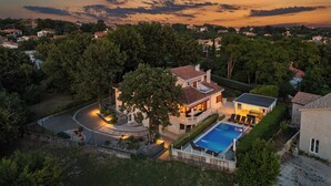 A large house with a swimming pool, surrounded by trees and a well-maintained garden.
