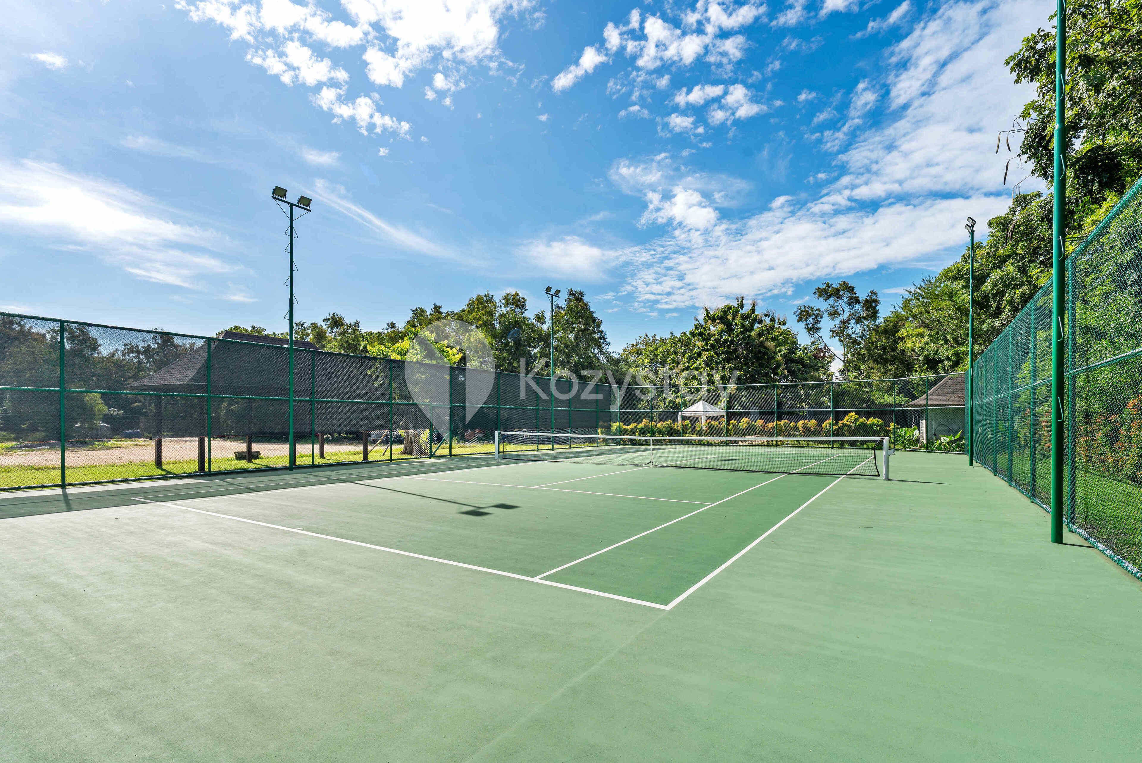 Una cancha de tenis al aire libre con vallas verdes y un cielo despejado.