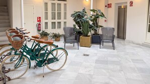Een ruime, overdekte ruimte met betegelde vloer, een groene fiets, rieten stoelen en potplanten.