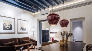 Ein modernes Wohnzimmer mit einem braunen Sofa, einem Couchtisch und einem Esstisch mit Stühlen. Zwei Pendelleuchten befinden sich über dem Tisch und eine Stehlampe steht neben dem Sofa.