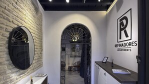 A modern interior with a brick wall, a reception desk, and a sign for 'Refinadores Apartments'.