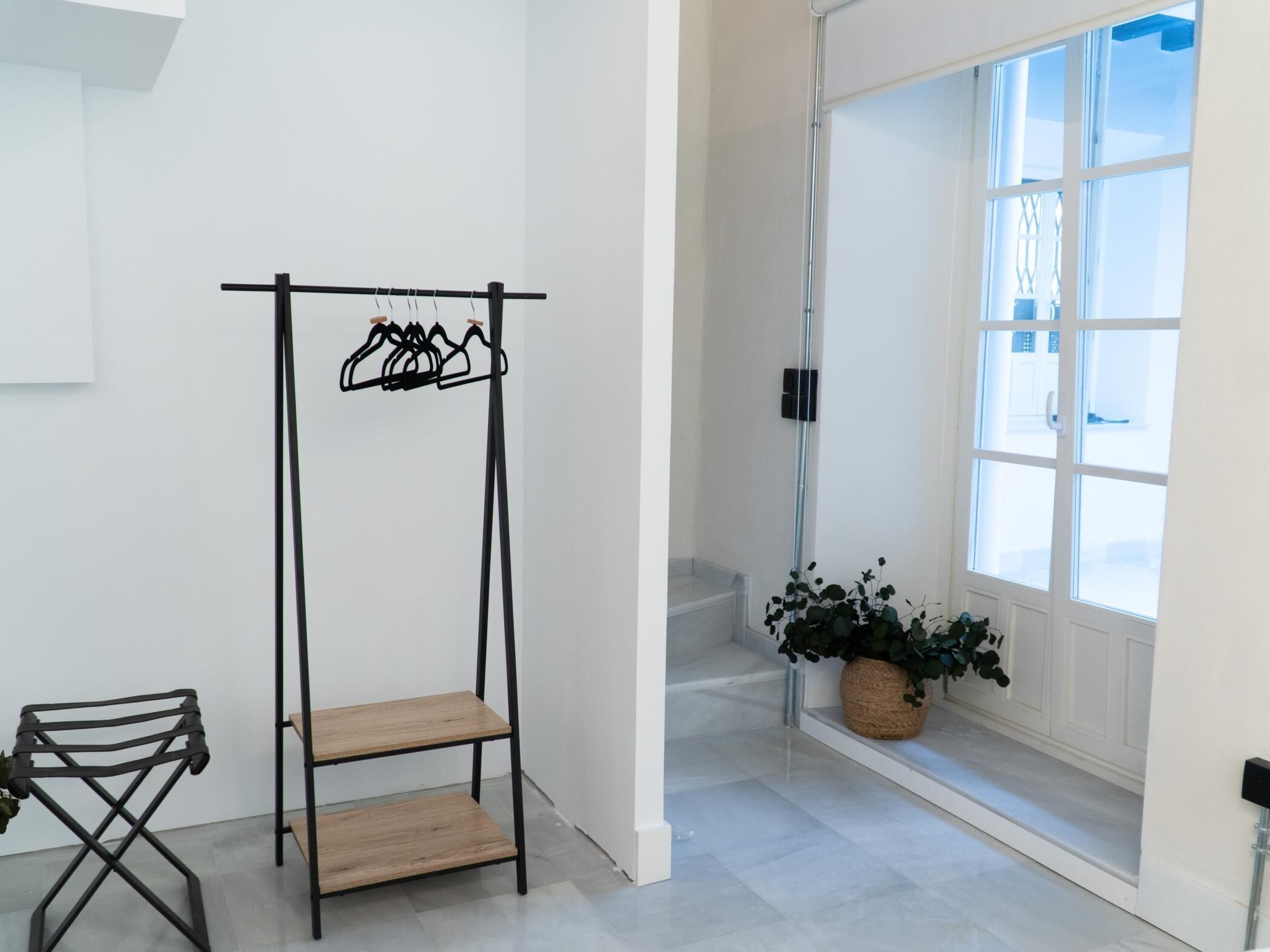 A room with a black metal shelf unit, a wooden chair, a potted plant, and a large window with a view of the outside.