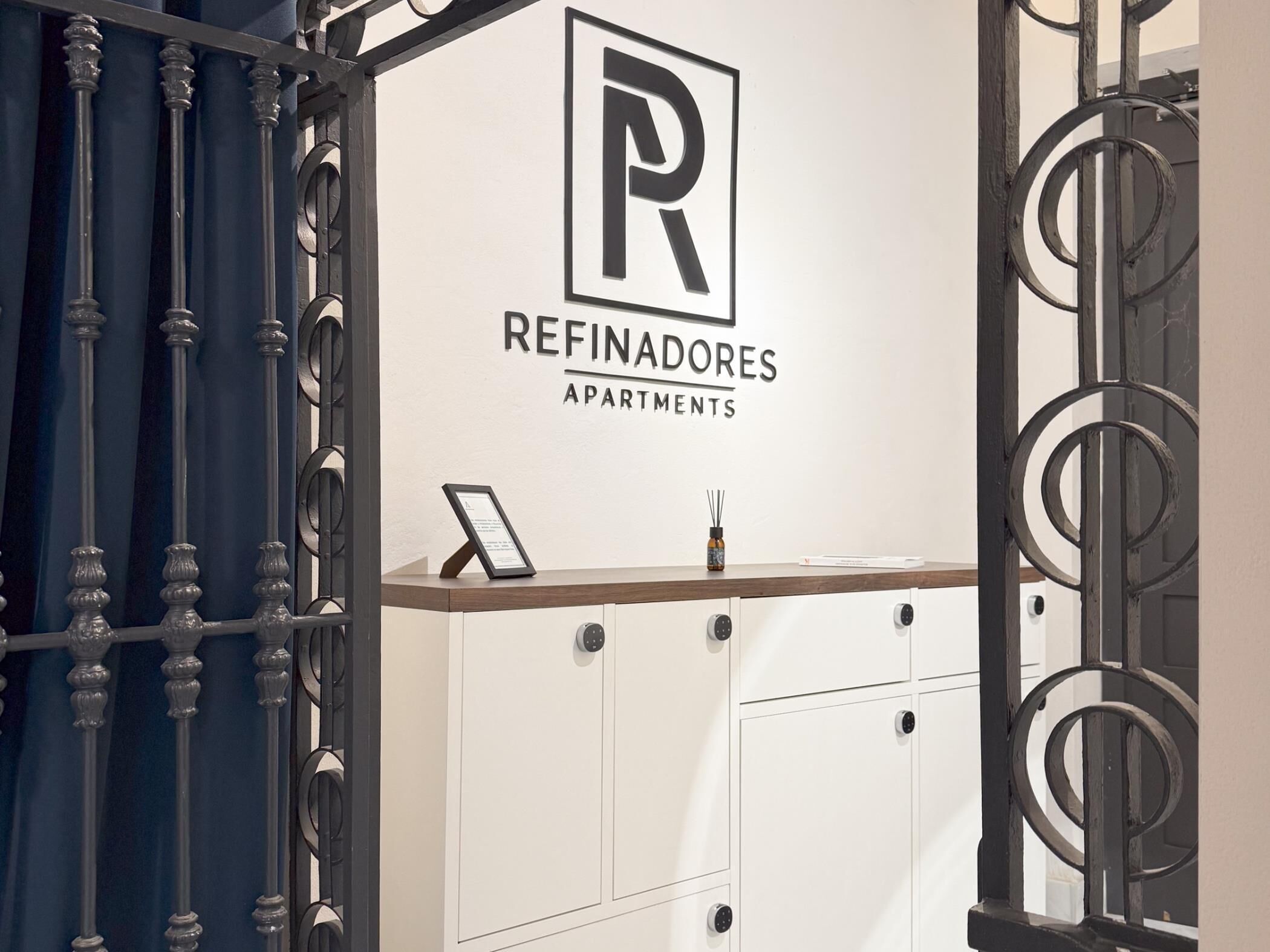 A modern apartment complex entrance with a sign reading "REFINADORES APARTMENTS".