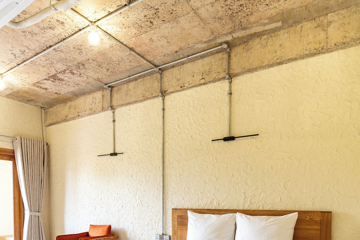 Una cama de madera grande con ropa blanca en una habitación con pared texturizada y techo de madera.