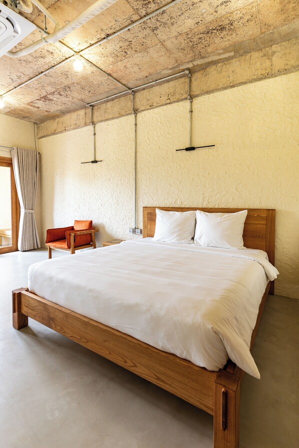 Una cama de madera grande con ropa blanca en una habitación con pared texturizada y techo de madera.
