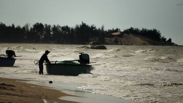 Escena de playa con dos barcos y una persona de pie en la orilla.