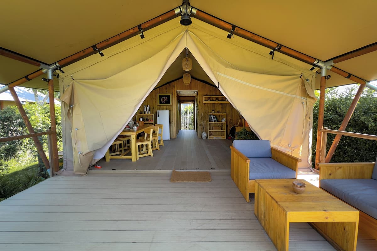 Alojamiento en carpa con terraza de madera, zona de estar y vistas al follaje circundante.