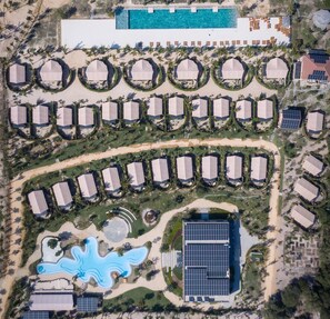 An aerial view of a resort with multiple bungalow-style accommodations, a central swimming pool, and a solar power installation. - WoCAL Resort Ke Ga (Tan Thanh)
