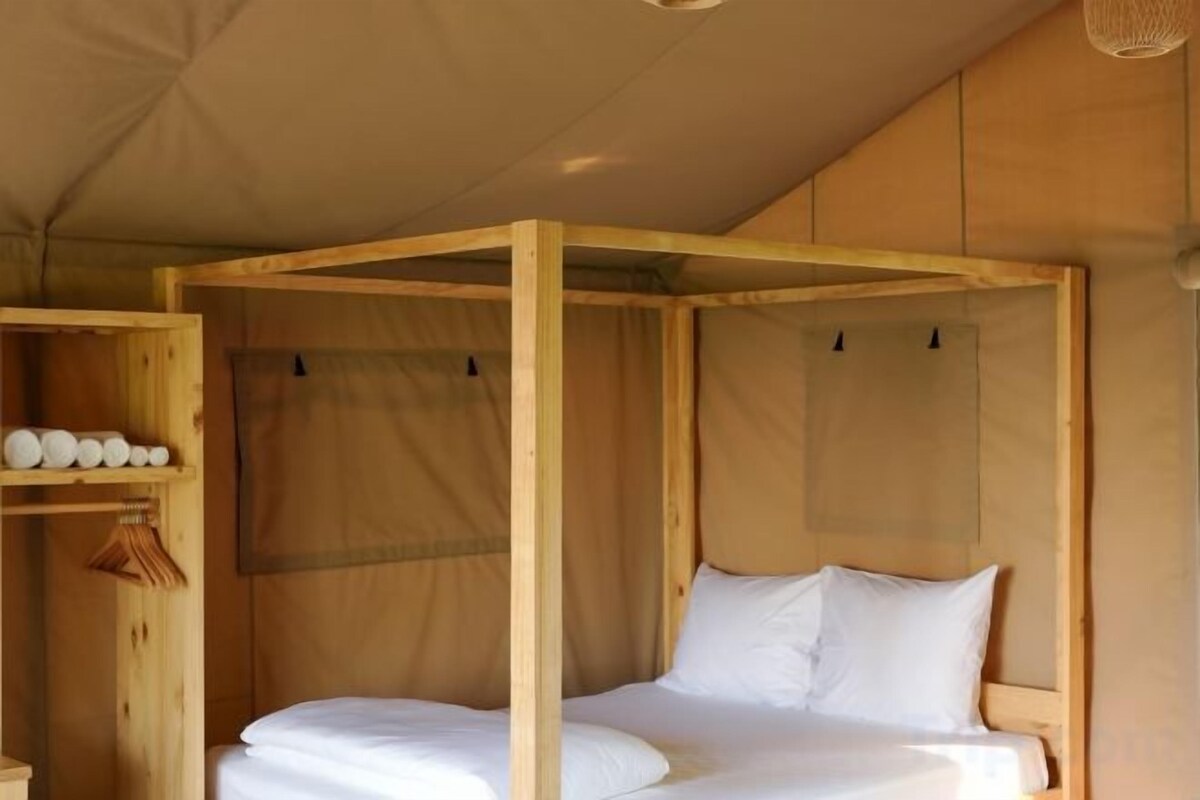Un lit simple avec un cadre en bois et du linge de lit blanc, installé dans une structure ressemblant à une tente.