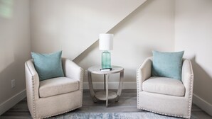 Dos sillones con cojines color turquesa, una mesita redonda con una lámpara turquesa y un techo inclinado.