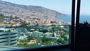 A view from a window overlooking a coastal city with a mix of residential and commercial buildings, a hilly backdrop, and a clear sky. - Diamond Ocean View by LovelyStay (Funchal)