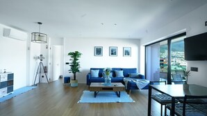 A modern living room with a blue sofa, a coffee table, and a large window offering a city view. - Diamond Ocean View by LovelyStay (Funchal)
