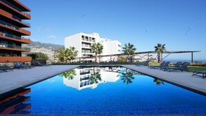 A swimming pool with lounge chairs, a white building, palm trees, and a clear sky. - Diamond Ocean View by LovelyStay (Funchal)