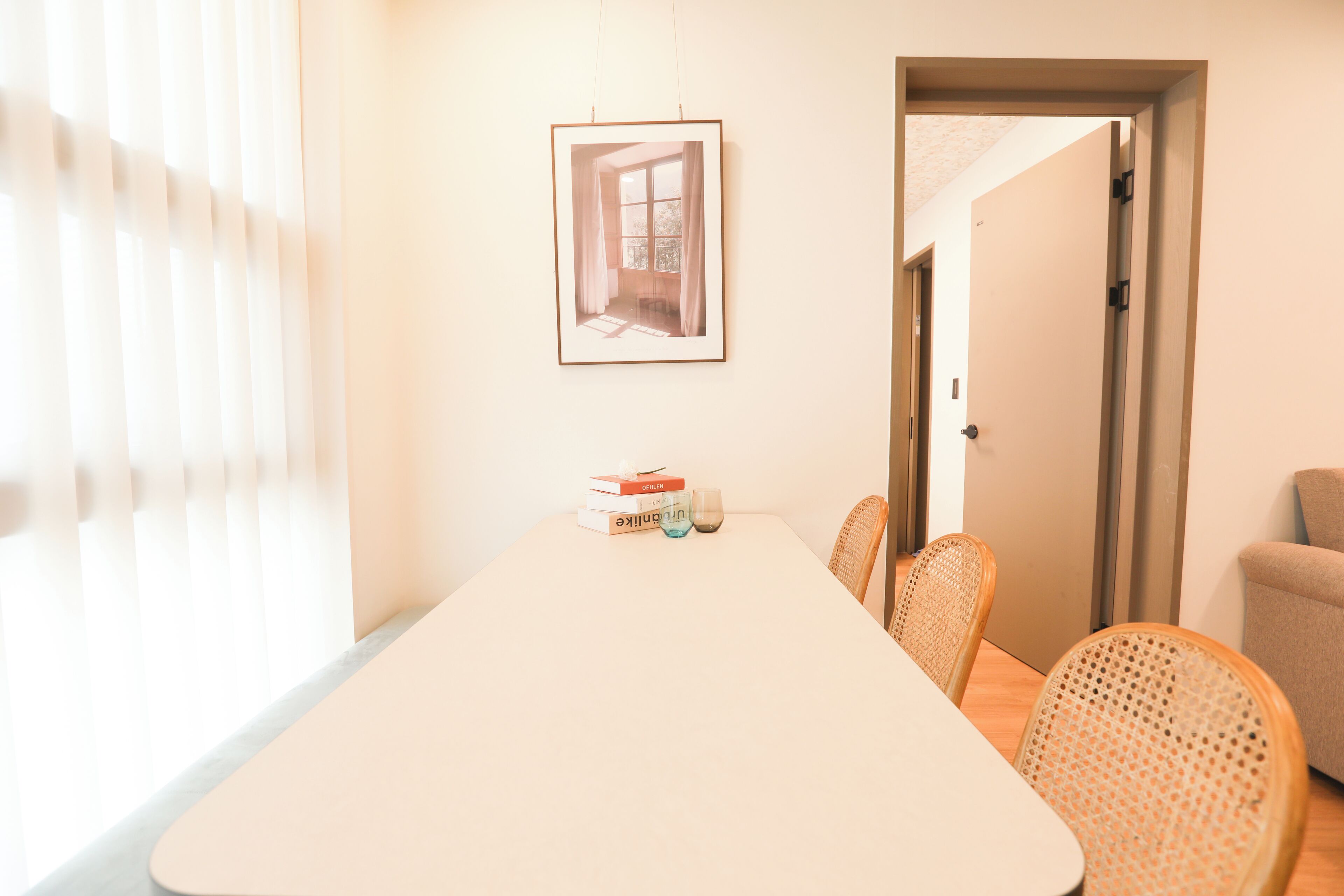 A dining area with a long table, chairs, a framed picture on the wall, and a door leading to another room.