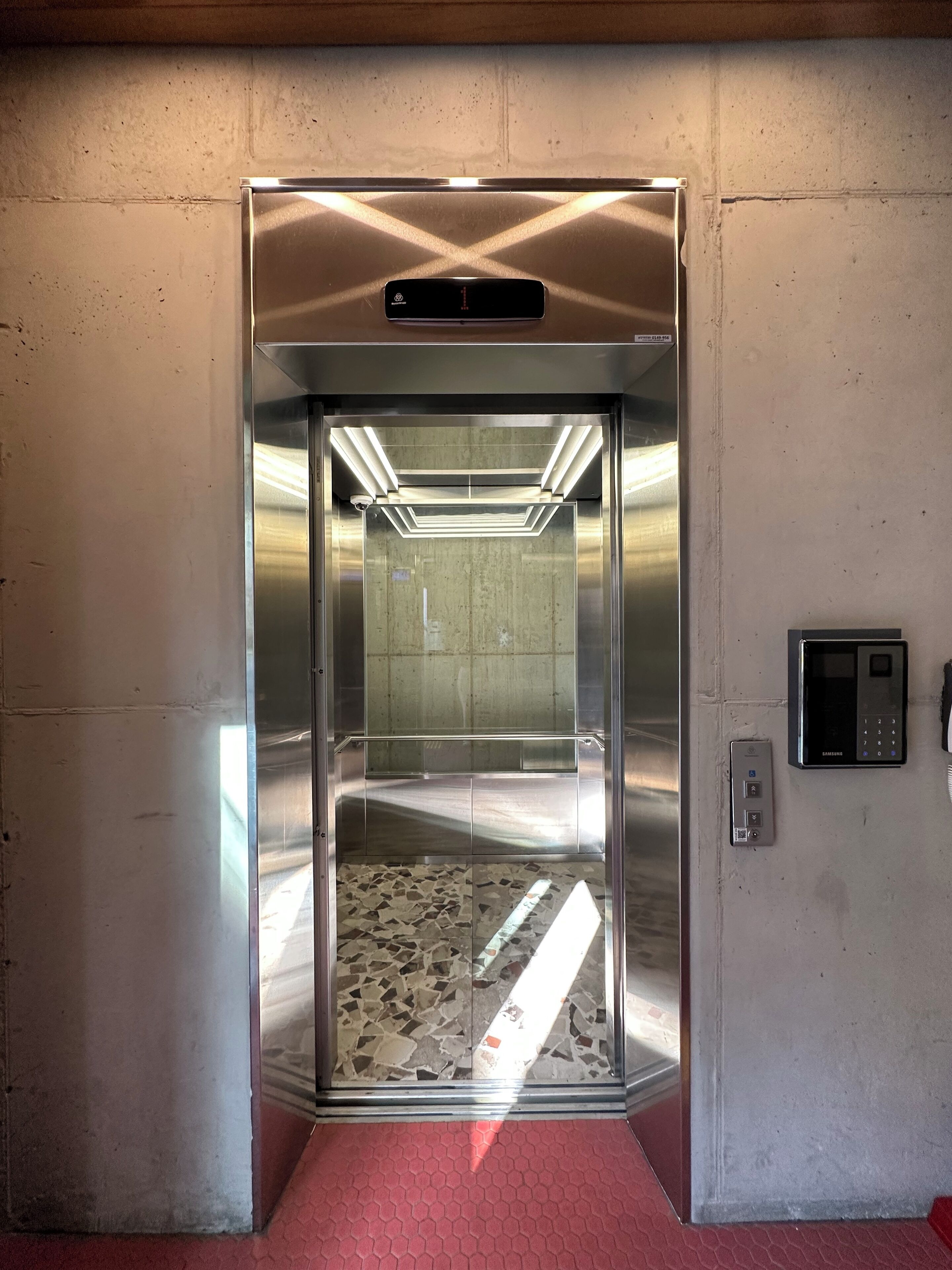 Un ascensor amb interior metàl·lic, un panell de control i un interfònic fixat a la paret.