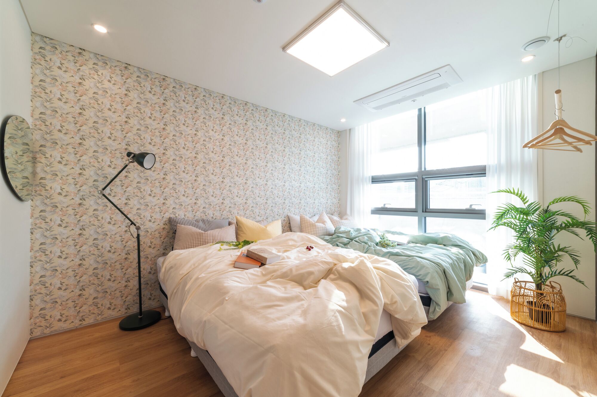 Un dormitorio con una cama grande, una lámpara de pie, una ventana con cortinas y una planta en maceta.