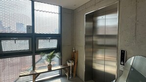 En moderne elevator med metallisk overflade, en betonvæg og et vindue med metalgitter.