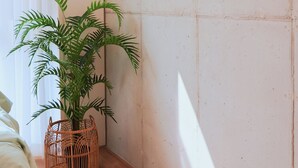 Et værelse med en seng, et tøjstativ, en potteplante og en fletkurv.