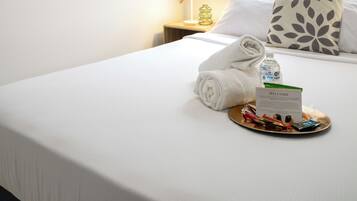 A hotel room with a neatly made bed, a welcome sign, a towel, and a tray with amenities.