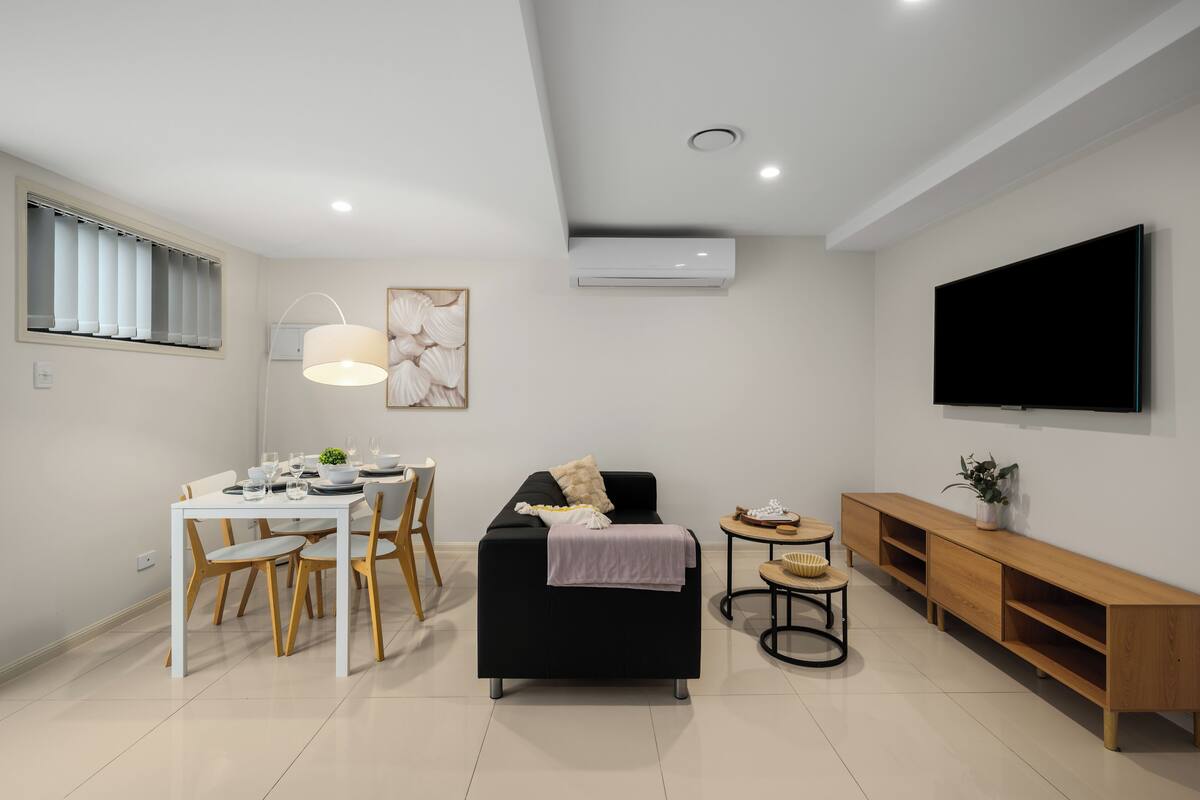 A modern living room with a dining area, a black sofa, a TV, and a wooden console.