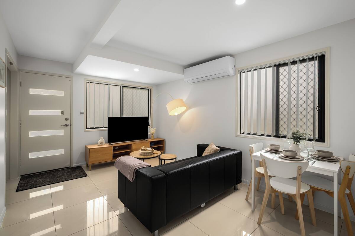 A modern living room with a black sofa, wooden dining table, and a TV.