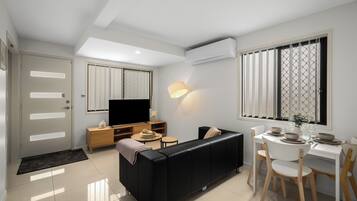 Una sala moderna con un sofá negro, una mesa de comedor de madera y un televisor.