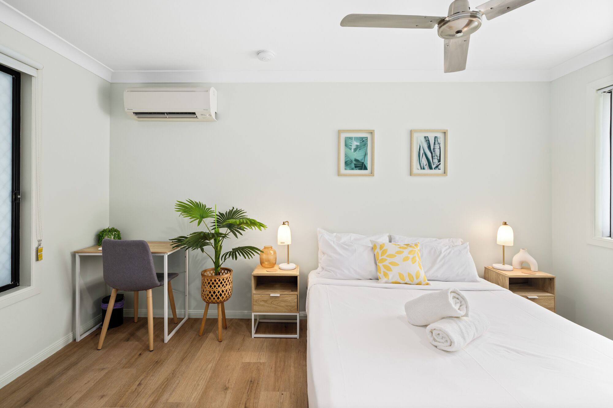 A hotel room with a bed, a desk, a chair, a plant, and two bedside lamps.