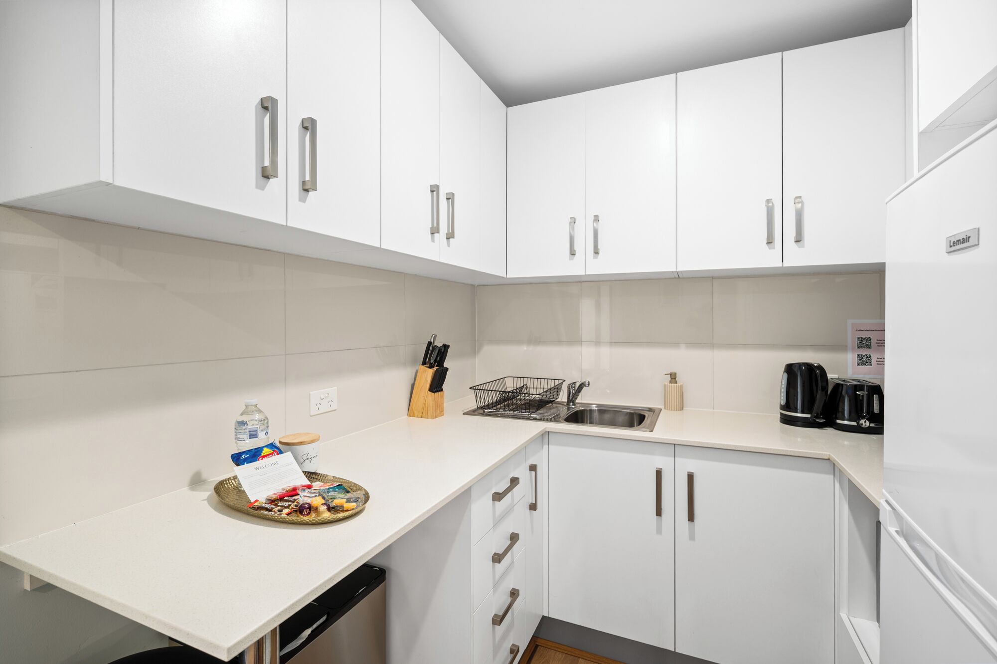 A modern kitchen with white cabinets, a stainless steel sink, and a coffee maker.