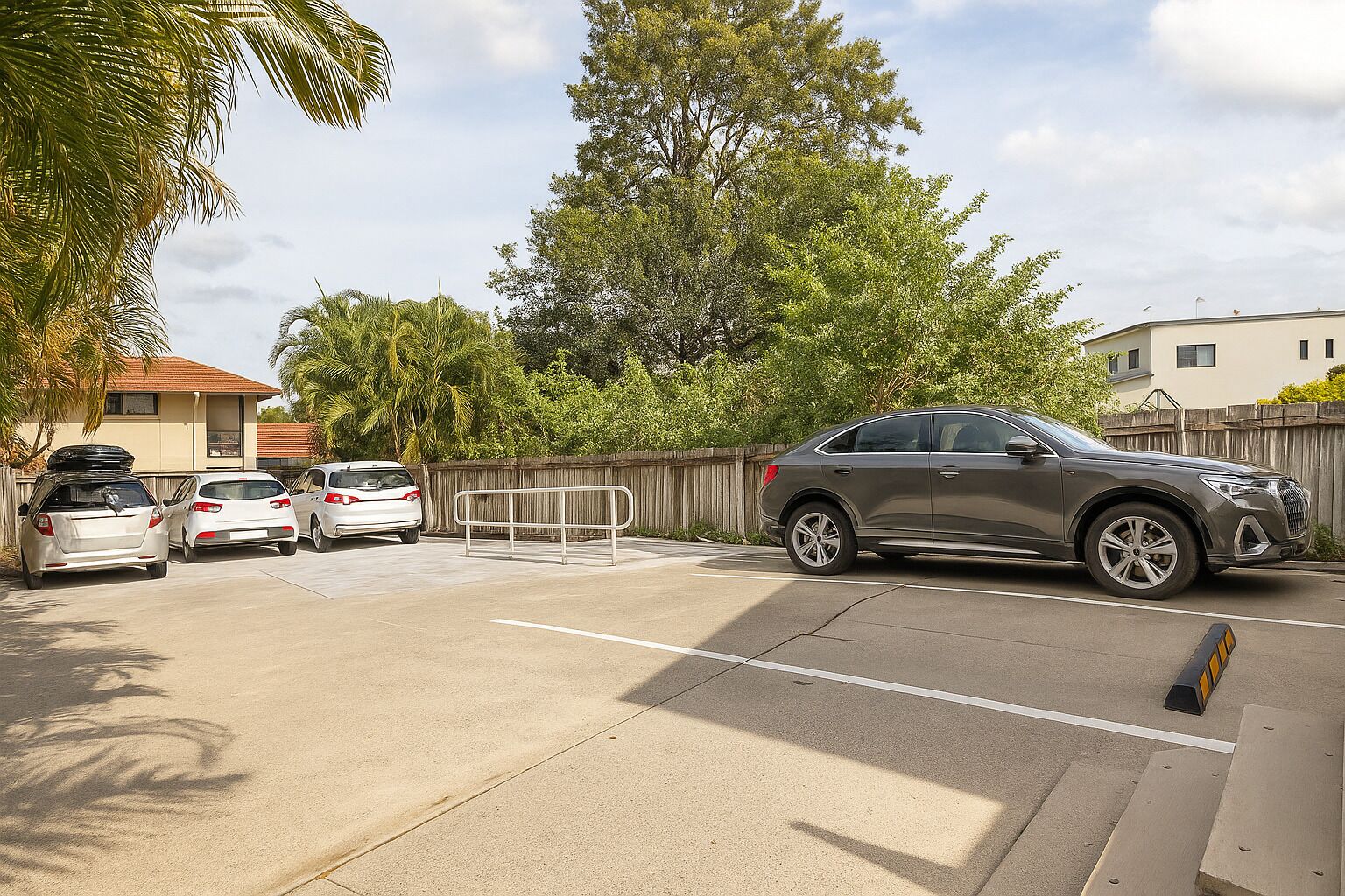 A parking lot with a gated entrance, a grey SUV, and three white cars parked.