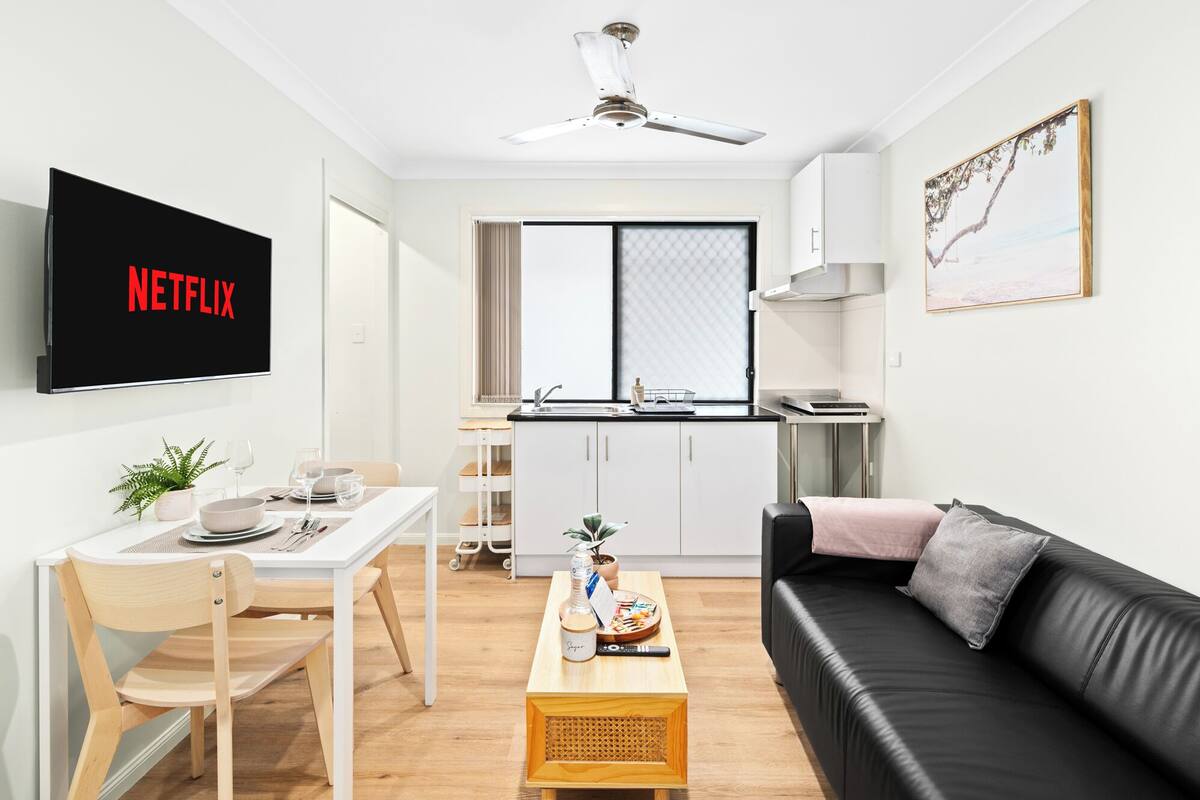 A compact living space with a dining area, kitchenette, and a black leather sofa.