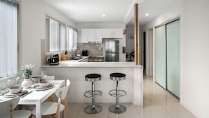 A modern kitchen with white cabinets, a stainless steel refrigerator, and a central island with bar stools. - Smart Suites Self Check-in Apartments - 144 Dixon (Sunnybank)