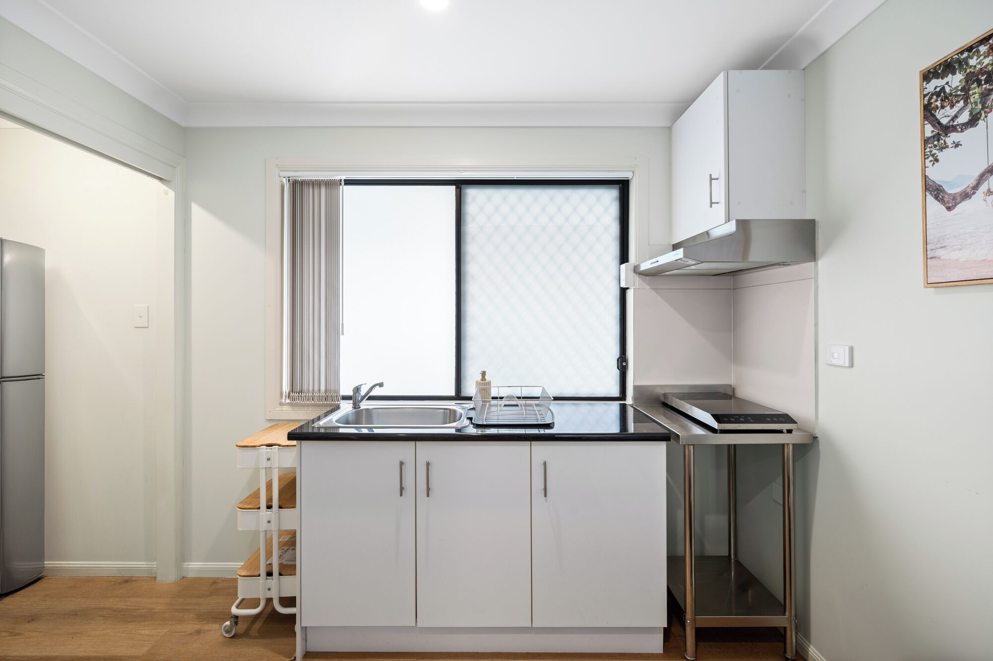 A compact kitchen with a built-in oven, a sink, and a window with blinds.