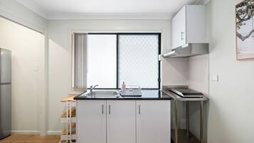 A compact kitchen with a built-in oven, a sink, and a window with blinds.