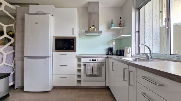 Una cocina moderna con microondas, horno y pileta integrados. Hay un refrigerador a la izquierda y una ventana a la derecha.
