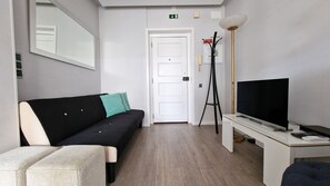 A modern hotel room with a black sofa, teal cushions, a white desk with a flat-screen TV, and a standing lamp. - Pino's Getaway by LovelyStay (Funchal)