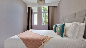 A bedroom with a large bed, a window with curtains, and a view of greenery outside. - Pino's Getaway by LovelyStay (Funchal)