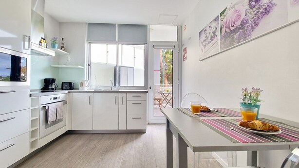 A modern kitchen with white cabinets, a coffee maker, and a dining area with a table set for breakfast. - Pino's Getaway by LovelyStay (Funchal)