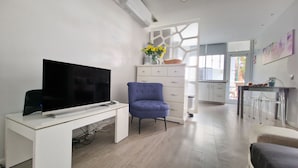 A modern living room with a flat-screen TV on a white table, a blue armchair, and a white dresser with a vase of flowers. - Pino's Getaway by LovelyStay (Funchal)