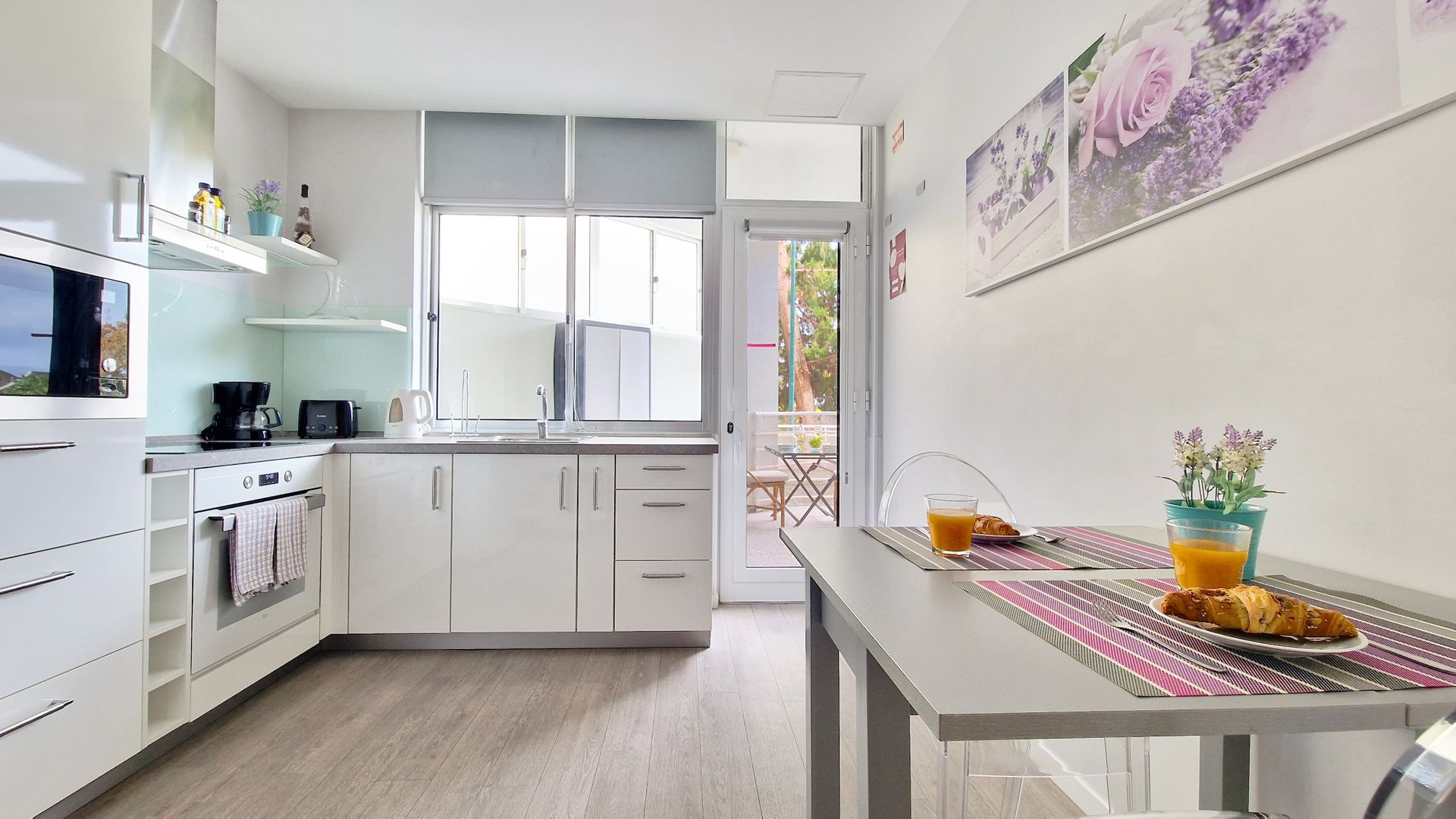 A modern kitchen with white cabinets, a coffee maker, and a dining area with a table set for breakfast.