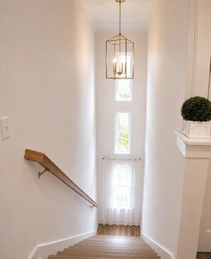 Un escalier avec une rampe en bois, un luminaire suspendu et une plante en pot.