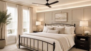 Un dormitorio con cama, mesitas de noche, ventilador de techo, planta en maceta y ventana con cortinas.