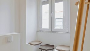 Habitació d'angle amb finestra, dos tamborets i una escala de fusta.