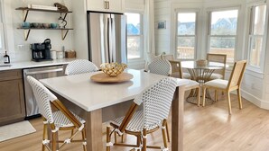 A modern kitchen with white cabinets, a stainless steel refrigerator, and a coffee maker. There is a dining area with a round table and four chairs. - Cabell’s Coastal Cottage-Sleeps 10 Jockey’s Ridge 1 mile to beach Sunsets & Pets (Nags Head)