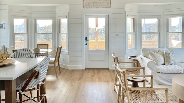 A cozy cottage interior with a dining area, a living room, and a door labeled "COTTAGE." - Cabell’s Coastal Cottage-Sleeps 10 Jockey’s Ridge 1 mile to beach Sunsets & Pets (Nags Head)