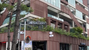 Un immeuble à plusieurs étages, sur lequel on peut lire l’inscription « US GALLERY », qui présente un design architectural moderne avec de grandes fenêtres et une façade en briques.